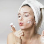 funny woman in a towel on the head happy cleanses the skin with foam on a white background isolated. Skincare cleansing concept