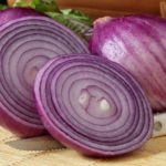 Freshly washed red onions on a woven mat with knife.  Salad gree