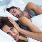 Portrait of woman blocking ears with hands while man snoring on