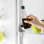 Hand of young woman taking bottle with soy sauce from fridge