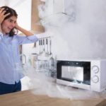 88554150-unhappy-young-woman-looking-at-smoke-emitting-through-microwave-oven-in-kitchen