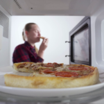 using-microwave-for-reheating-food-baked-pizza-on-a-plate-inside-the-microwave-in-the-background-girl-eats-slice-of-heated-pizza_s00dljqgx_thumbnail-full01