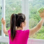 Asian woman cleaning a window with green cloth at home.