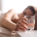 woman-in-bed-reaching-for-glass-of-water-to-drink-before-going-to-sleep